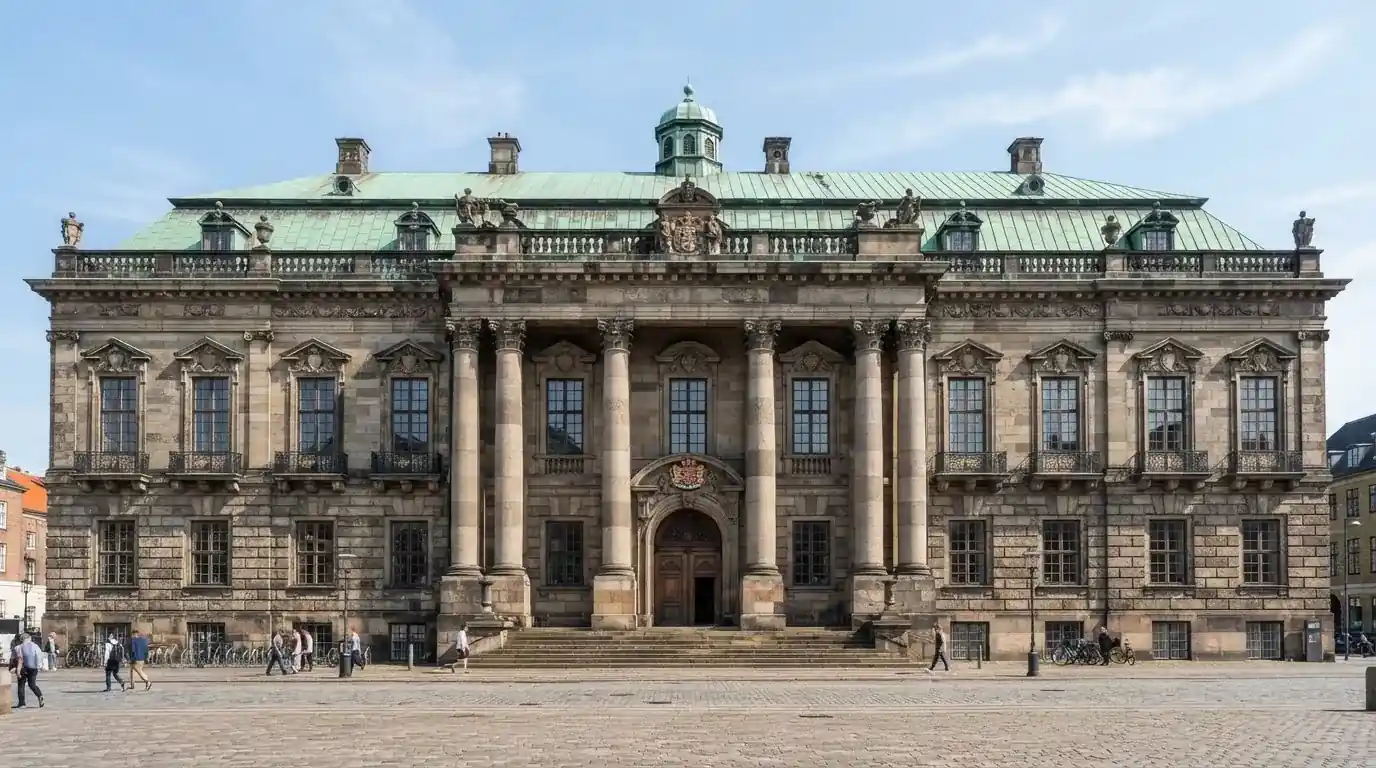 En historisk bygning i København med grøn kobbertag og kolonner i klart dagslys, set fra pladsen foran.